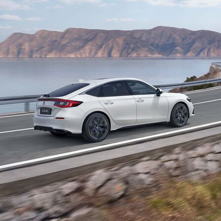 Vue latérale de la Honda Civic e:HEV roulant sur une route côtière.